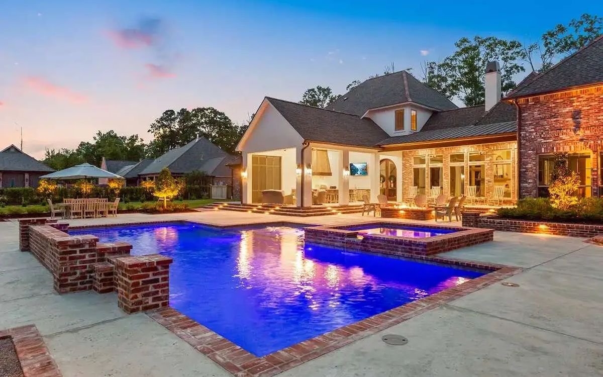 Lit outdoor living room beside a gunite pool at dusk